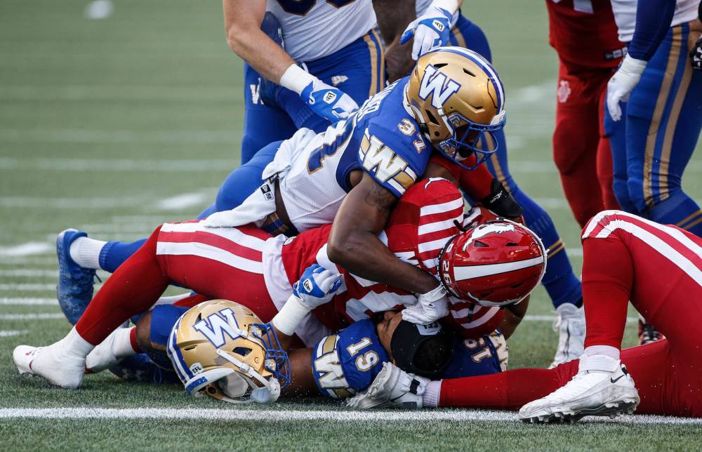 Winnipeg Blue Bombers' Brandon Alexander (37) and Kyrie Wilson (19) stop Calgary Stampeders' Dedrick Mills (26) from scoring the touchdown during first half CFL action in Winnipeg, Friday, July 12, 2024. THE CANADIAN PRESS/John Woods