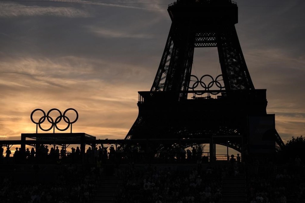 Spectators watch a quarterfinal beach volleyball match between Australia and Switzerland at sunset at Eiffel Tower Stadium at the 2024 Summer Olympics, Tuesday, Aug. 6, 2024, in Paris, France. (AP Photo/Robert F. Bukaty)