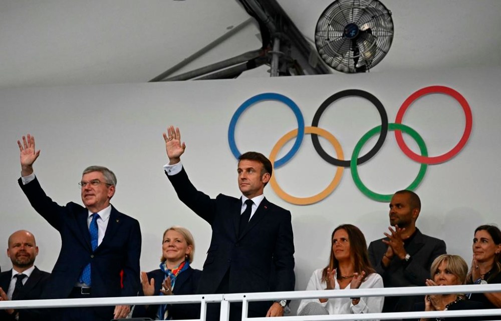 France's President Emmanuel Macron, center, and IOC President Thomas Bach, left, wave as they arrive to attend the opening ceremony for the 2024 Summer Olympics in Paris, France, Friday, July 26, 2024. (Loic Venance/Pool Photo via AP)