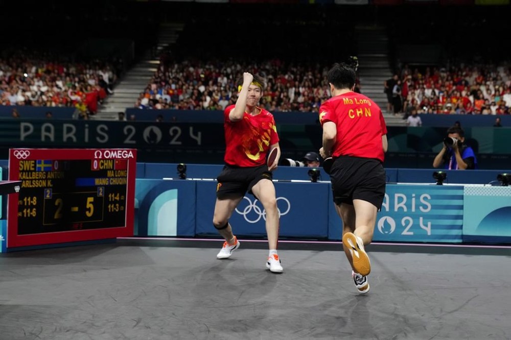 China's Wang Chuqin, left, and Ma Long react after a winning set against Sweden's Anton Kallberg and Kristian Karlsson during the men's gold medal team table tennis match at the 2024 Summer Olympics, Friday, Aug. 9, 2024, in Paris, France. (AP Photo/Petros Giannakouris)