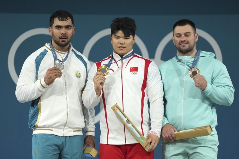 Medalists, from left to right, Akbar Djuraev of Uzbekistan, silver, Liu Huanhua of China, gold, and Individual Neutral Athlete Yauheni Tsikhantsou, bronze, celebrate on the podium during the medal ceremony for the men's 102kg weightlifting event at the 2024 Summer Olympics, Saturday, Aug. 10, 2024, in Paris, France. (AP Photo/Kin Cheung)