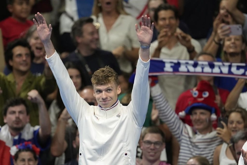 Leon Marchand of France, waves as he stands on the podium to receive his gold medal for the men's 200-meter individual medley final at the 2024 Summer Olympics, Friday, Aug. 2, 2024, in Nanterre, France. (AP Photo/Ashley Landis)