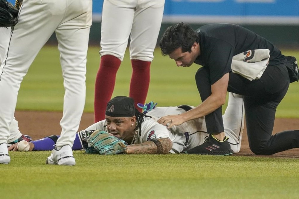 Arizona Diamondbacks' Ketel Marte, center bottom, is looked at by head athletic trainer Ryan DiPanfilo, right, after a collision at second base with Philadelphia Phillies' Garrett Stubbs during the fourth inning of a baseball game Saturday, Aug 10, 2024, in Phoenix. (AP Photo/Darryl Webb)