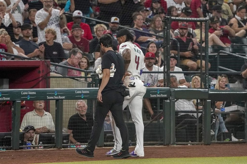 CORRECTS TO ASSISTANT ATHLETIC TRAINER MAX ESPOSITO NOT HEAD ATHLETIC TRAINER RYAN DIPANFILO - Arizona Diamondbacks' Ketel Marte (4) is walked off the field by assistant athletic trainer Max Esposito, left, after a collision at second base with Philadelphia Phillies' Garrett Stubbs during the fourth inning of a baseball game Saturday, Aug 10, 2024, in Phoenix. (AP Photo/Darryl Webb)