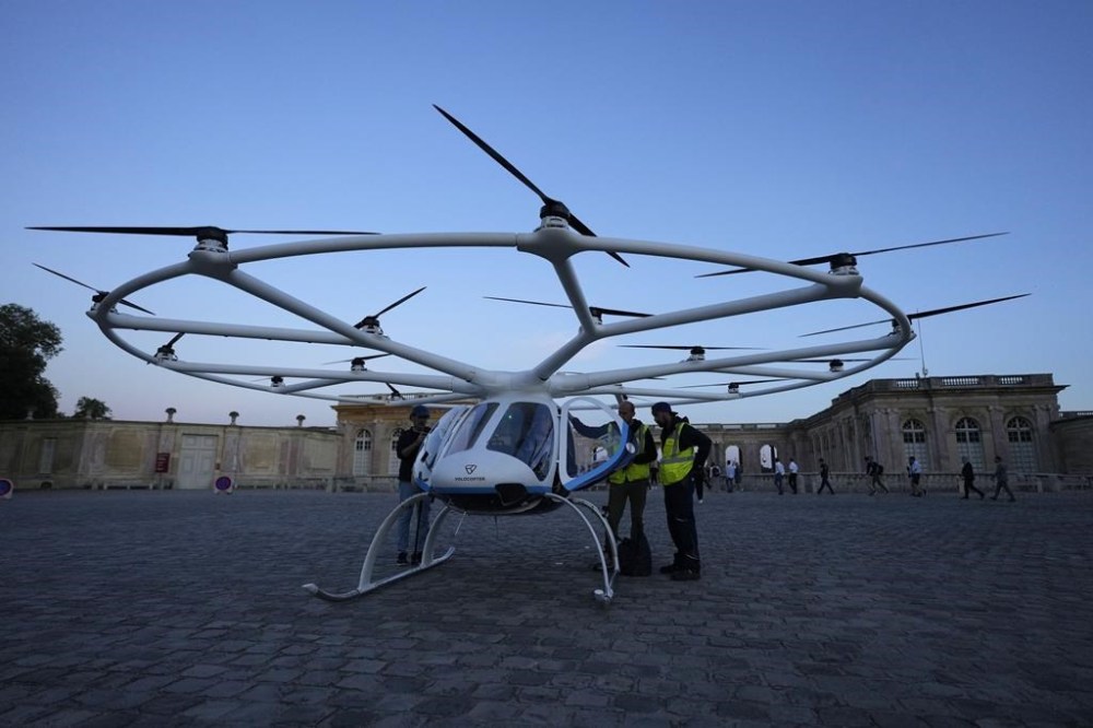 People gather at a Volocopter aircraft before a test flight on the last day of the 2024 Olympics at the 2024 Summer Olympics, Sunday, Aug. 11, 2024, in Versailles, France. (AP Photo/Mosa'ab Elshamy)