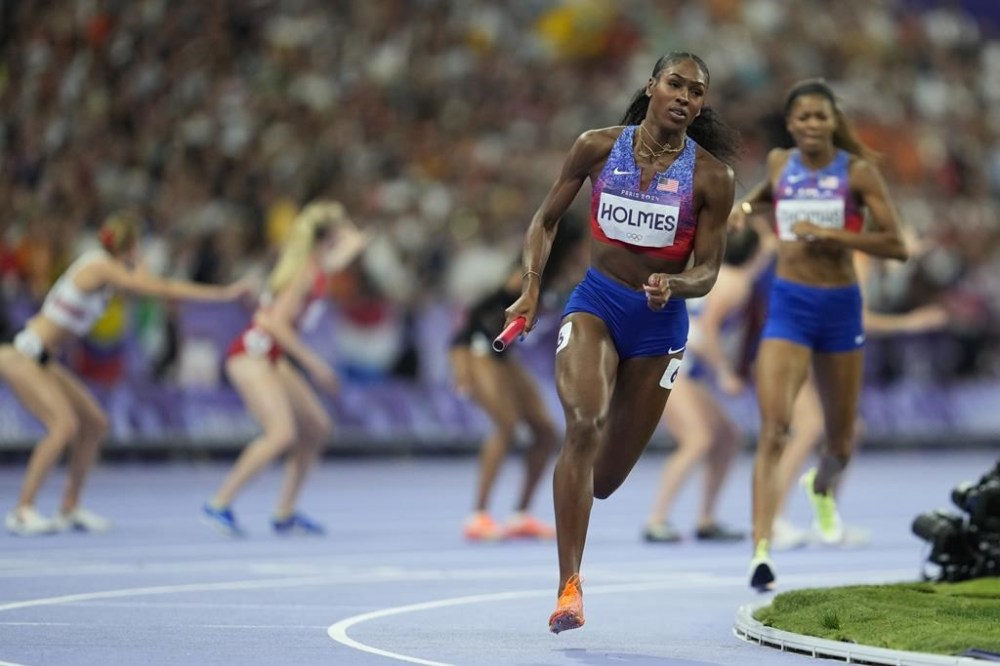 Alexis Holmes runs after taking over the baton from teammate Gabby Thomas, right, to win the gold medal in the women's 4 x 400 meters relay final at the 2024 Summer Olympics, Saturday, Aug. 10, 2024, in Saint-Denis, France. (AP Photo/Ashley Landis)