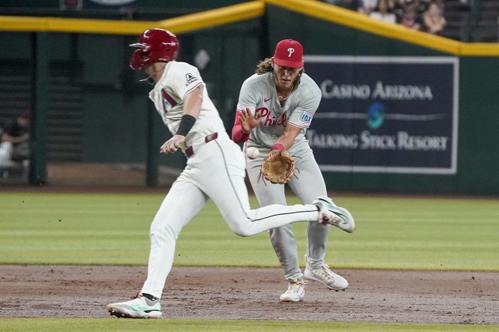 Arizona Diamondbacks' Kevin Newman, left, runs in front of Philadelphia Phillies third base Alec Bohm as Bohm fields the ball during the second inning of a baseball game Sunday, Aug. 11, 2024, in Phoenix. (AP Photo/Darryl Webb)