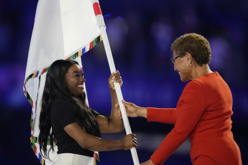 Los Angeles Mayor Karen Bass hands the Olympic flag to United States' gymnast Simone Biles during the 2024 Summer Olympics closing ceremony at the Stade de France, Sunday, Aug. 11, 2024, in Saint-Denis, France. (AP Photo/Natacha Pisarenko)