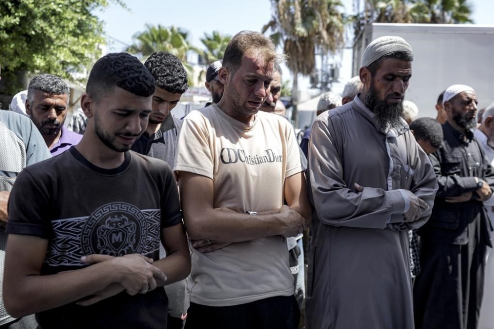 Mohammad Abu Al-Qumsan, Center, prays next to the bodies of his 4-day-old twin children, killed in the Israeli bombardment of the Gaza Strip, at a hospital in Deir al-Balah, Tuesday, Aug. 13, 2024. (AP Photo/Abdel Kareem Hana)