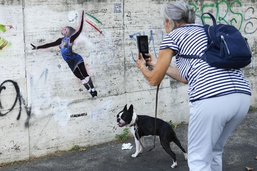 A woman takes a picture at Laika's street-art celebration of Paola Egonu, who helped lead Italy to its first-ever Olympic gold medal in women's volleyball, in Rome, Wednesday, Aug. 14, 2024. A day after images of the graffiti began circulating, someone painted over Laika's original work, turning Egonu's dark skin pink and blurring out the words on the volleyball. At some point on Tuesday, someone used a dark marker to try to restore Laika's original design. (AP Photo/Gregorio Borgia)