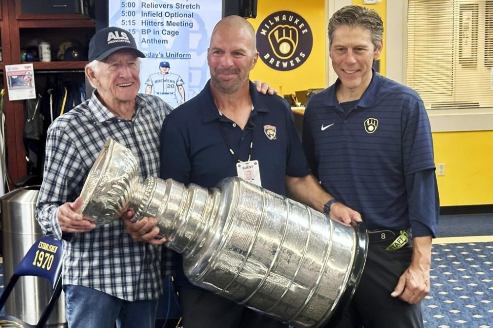 Longtime Milwaukee Brewers broadcaster Bob Uecker, left, Florida Panthers general manager Bill Zito, and Brewers director of clubhouse operations Tony Migliaccio pose with the Stanley Cup in the team's clubhouse before a baseball game against the Los Angeles Dodgers, Wednesday, Aug. 14, 2024, in Milwaukee. (AP Photo/Steve Megargee)