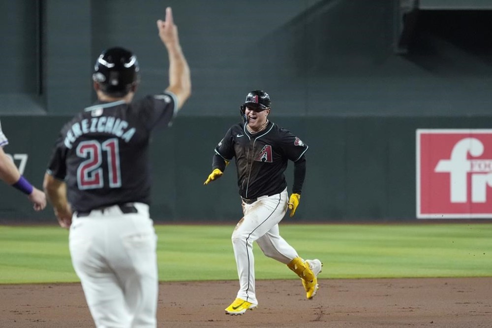 Arizona Diamondbacks' Joc Pederson, right, laughs as he runs to third base as Diamondbacks third base coach Tony Perezchica (21) waves Pederson home after a double and a two-base error during the first inning of a baseball game against the Colorado Rockies, Wednesday, Aug. 14, 2024, in Phoenix. (AP Photo/Ross D. Franklin)