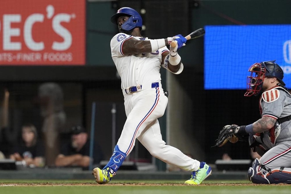 Texas Rangers right fielder Adolis Garcia follows through on a single as Minnesota Twins catcher Christian Vazquez, right, looks on in the fifth inning of a baseball game, Thursday, Aug. 15, 2024, in Arlington, Texas. (AP Photo/Tony Gutierrez)