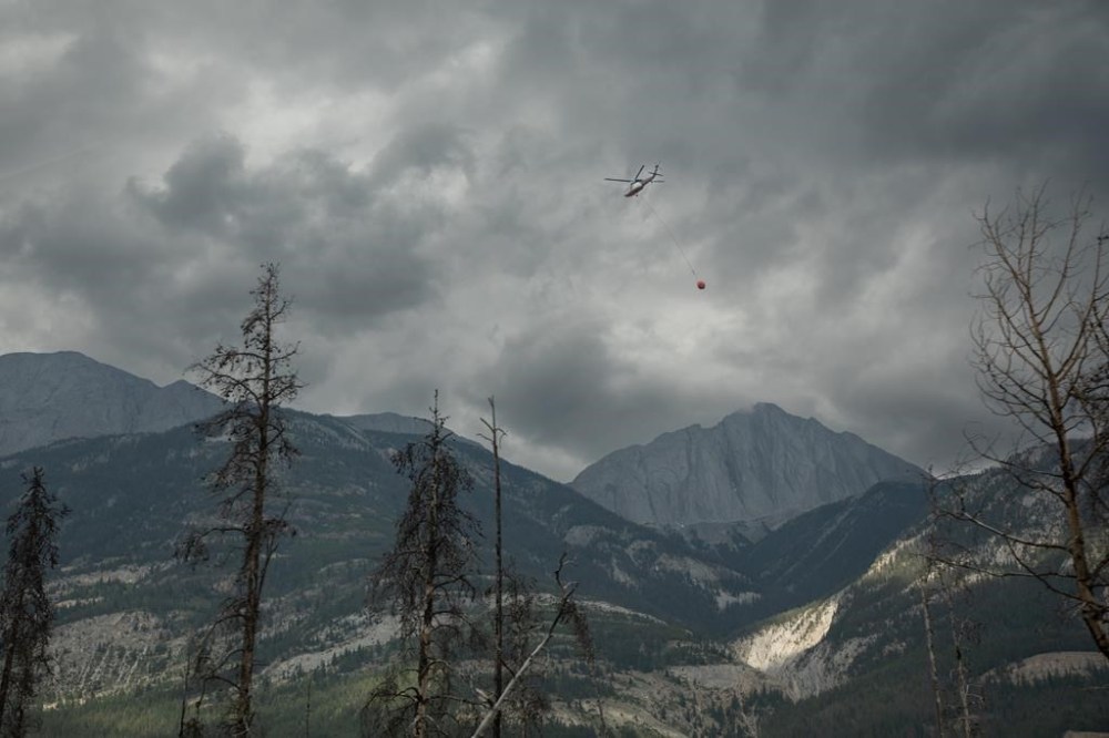 A helicopter buckets water onto smouldering fires outside of Jasper, Alta., on Friday July 26, 2024. It could take more than a century for the freshly burned forest in Jasper National Park to regenerate into its previous postcard-perfect form, a wildfire expert says. THE CANADIAN PRESS/Amber Bracken