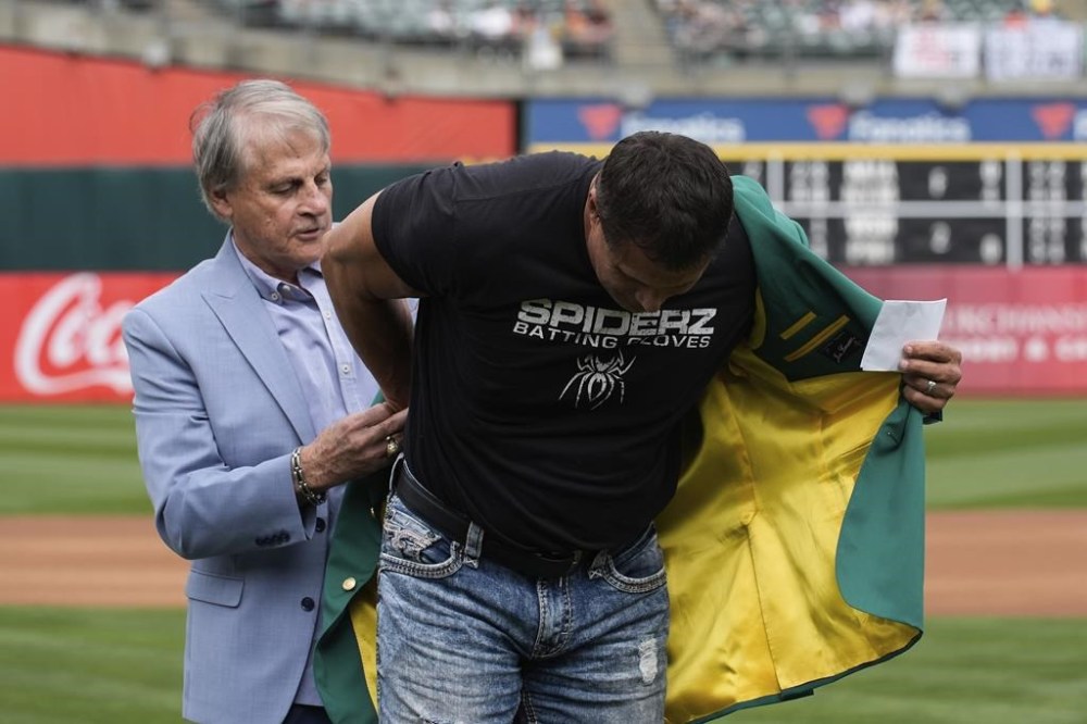 Former Oakland Athletics player Jose Canseco, right, is helped into his green jacket by Tony La Russa, left, after being inducted into the team's Hall of Fame before a baseball game against the San Francisco Giants, Saturday, Aug. 17, 2024, in Oakland, Calif. (AP Photo/Godofredo A. Vásquez)