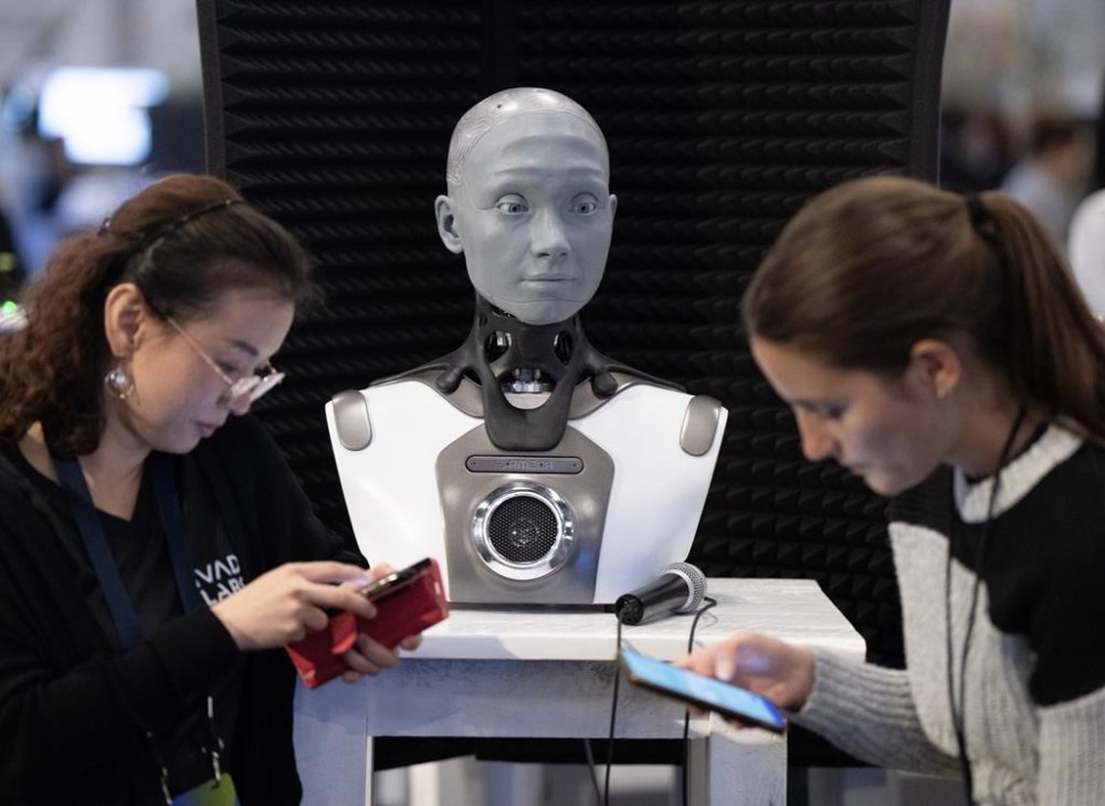 People check their phones as AMECA, an AI robot, looks on at the All In artificial intelligence conference, September 28, 2023 in Montreal. A federal advisory body is calling on Canada's security agencies to publish detailed descriptions of their current and intended uses of artificial intelligence systems and software applications.THE CANADIAN PRESS/Ryan Remiorz