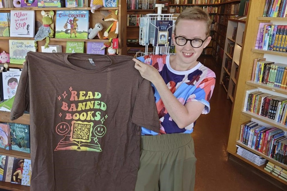 FILE - Former Norman High School English teacher Summer Boismier holds up a T-shirt with a QR code link to the Brooklyn Public Library at the Green Feather Book Company in Norman, Okla., on Oct. 6, 2022. (AP Photo/Sean Murphy, File)