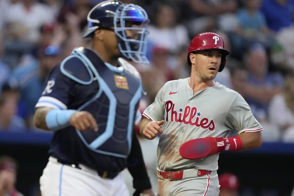 Philadelphia Phillies' J.T. Realmuto runs past Kansas City Royals catcher Salvador Perez to score on a single by Brandon Marsh during the third inning of a baseball game Friday, Aug. 23, 2024, in Kansas City, Mo. (AP Photo/Charlie Riedel)