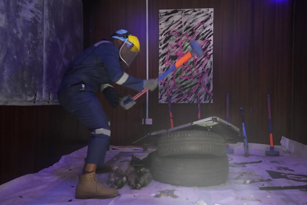 Olaribigbe Akeem, wearing protective gear, uses a sledgehammer to break a television set to vent his anger inside the Shadow Rage Room in Lagos, Nigeria, Sunday, July 28, 2024. (AP Photo/Sunday Alamba)