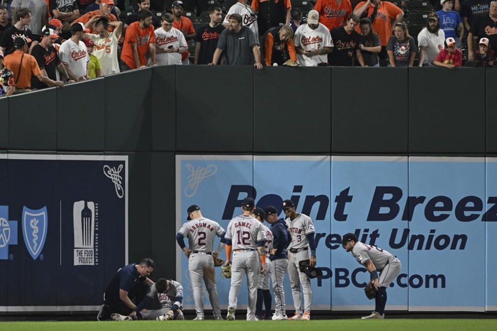 Houston Astros left fielder Mauricio Dubón sits on the ground and is seen by the trainer after running into the wall to make a catch during the seventh inning of a baseball game against the Baltimore Orioles, Sunday, Aug. 25, 2024, in Baltimore. (AP Photo/Terrance Williams)