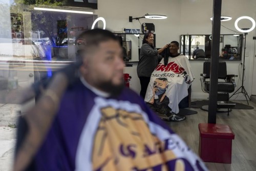 Adelita Valentine, owner of HairFreek Barbers, uses a towel to wipe away hair from the face of Cameron Loualhati in Los Angeles, Wednesday, Aug. 21, 2024. (AP Photo/Jae C. Hong)