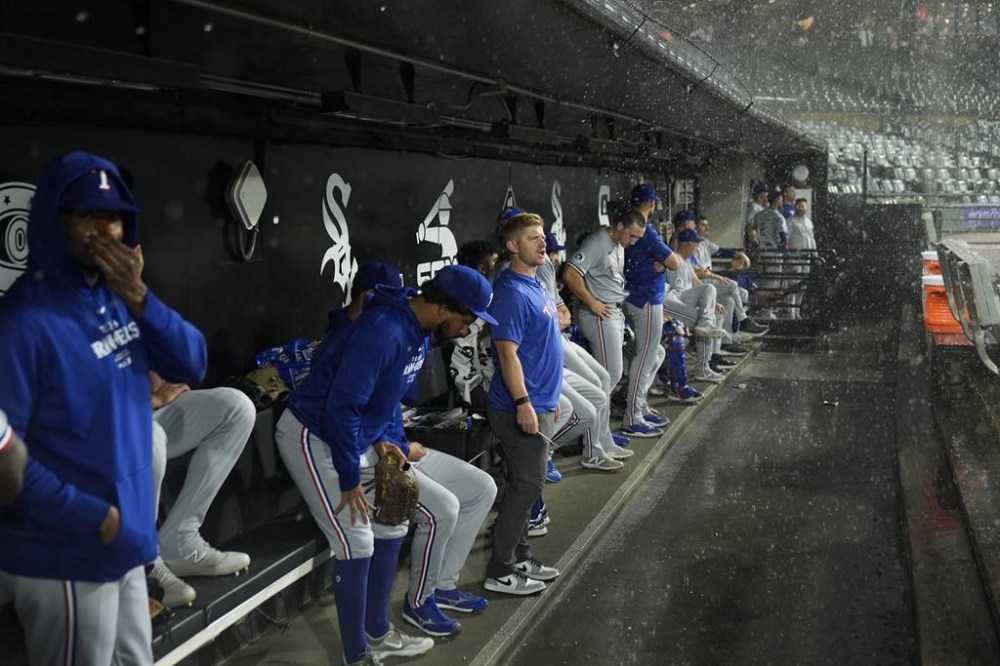 The Texas Rangers take shelter in the dugout as rain pours down during the first inning of a baseball game against the Chicago White Sox, Tuesday, Aug. 27, 2024, in Chicago. (AP Photo/Erin Hooley)
