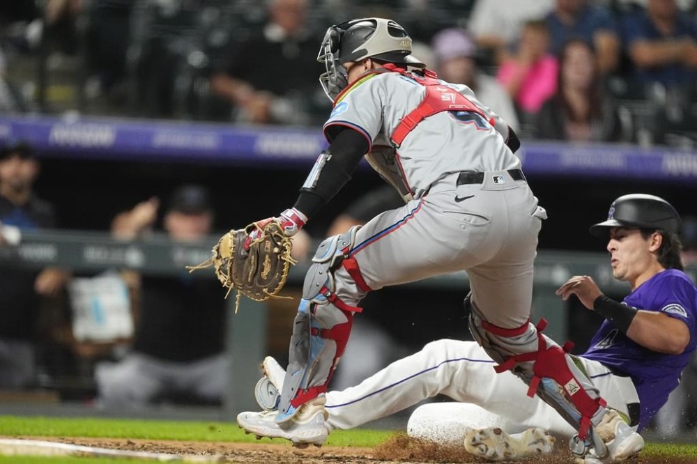 Miami Marlins catcher Nick Fortes, front, pursues an errant throw from shortstop Otto Lopez as Colorado Rockies' Michael Toglia, far right, scores in the sixth inning of a baseball game Wednesday, Aug. 28, 2024, in Denver. (AP Photo/David Zalubowski)