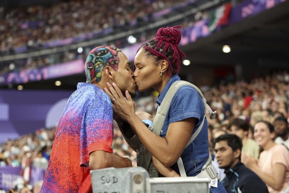 Roderick Townsend of the United States kisses his wife Tynita Townsend, with their son Rodney Townsend, between Rodrick's jumps in the T47 Men's High Jump at the 2024 Paralympics, Sunday, Sept. 1, 2024 in Paris, France. (AP Photo/Caleb Craig)