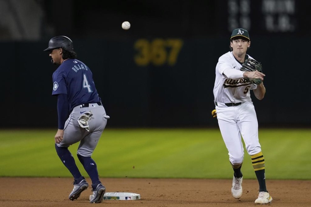 Oakland Athletics shortstop Jacob Wilson, right, turns a double play after forcing out Seattle Mariners' Josh Rojas (4) at second during the fifth inning of a baseball game Tuesday, Sept. 3, 2024, in Oakland, Calif. J.P. Crawford was out at first on the play. (AP Photo/Godofredo A. Vásquez)