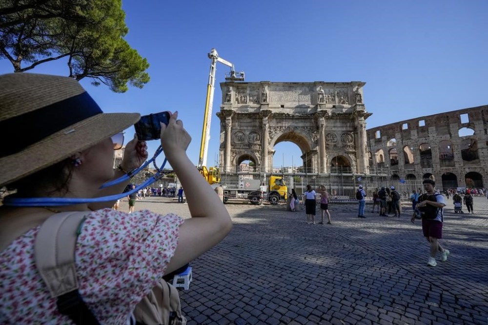 A tourist takes photos of the 315 A.D Arch of Constantine, near the Colosseum, in Rome, Wednesday, Sept. 4, 2024, as workers on site with cranes gather up fragments and secure broken areas of the arch after lightning struck it during a storm Tuesday, Sept. 3, loosening fragments from the ancient Roman structure. (AP Photo/Andrew Medichini)