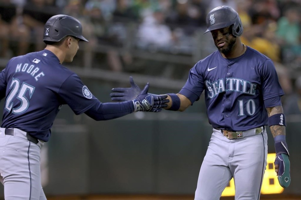 Seattle Mariners outfielder Victor Robles (10) is congratulated by Dylan Moore (25) after scoring on a single by Mitch Garver during the fourth inning of a baseball game against the Oakland Athletics in Oakland, Calif., Wednesday, Sept. 4, 2024. (AP Photo/Jed Jacobsohn)