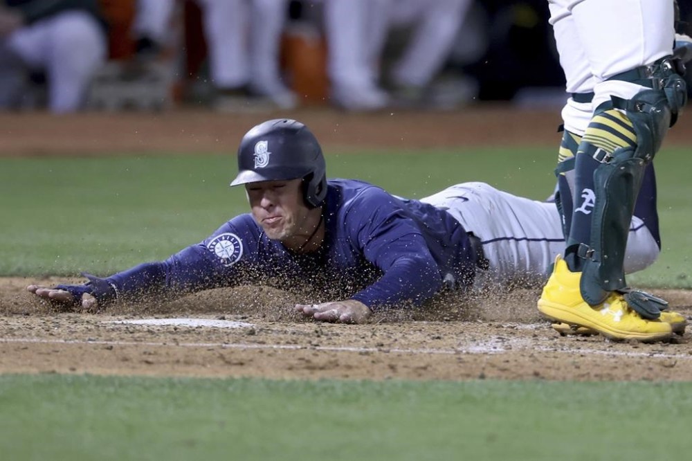 Seattle Mariners shortstop Dylan Moore (25) slides to home plate, safe on a single hit by Julio Rodríguez during the seventh inning of a baseball game against the Oakland Athletics in Oakland, Calif., Wednesday, Sept. 4, 2024. (AP Photo/Jed Jacobsohn)