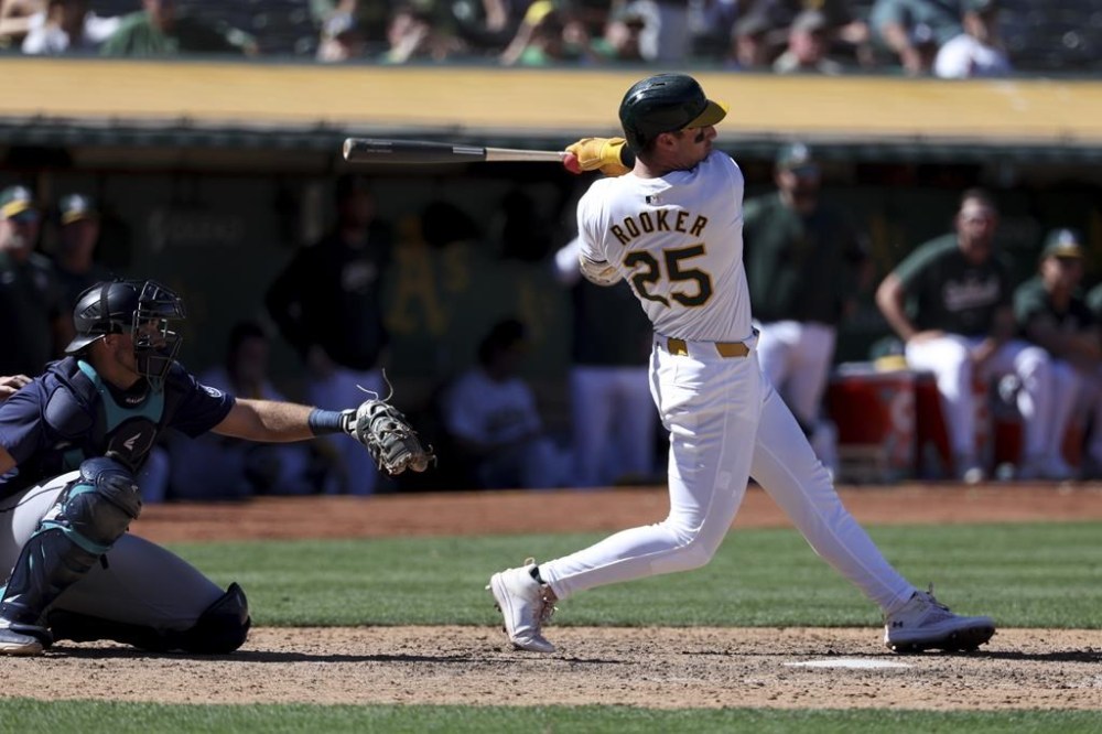 Oakland Athletics' Brent Rooker (25) hits a two-run run in front of Seattle Mariners catcher Cal Raleigh, left, during the ninth inning of a baseball game in Oakland, Calif., Thursday, Sept. 5, 2024. (AP Photo/Jed Jacobsohn)