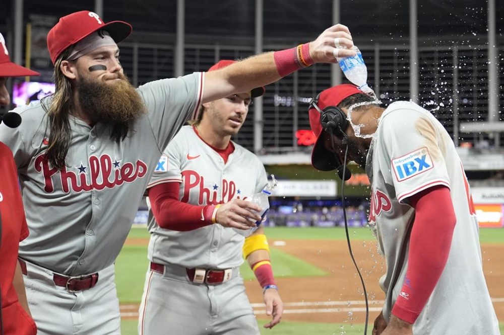 Philadelphia Phillies' Brandon Marsh, left, and Bryson Stott, center, douse Johan Rojas, right, as he is interviewed after a baseball game against the Miami Marlins, Friday, Sept. 6, 2024, in Miami. (AP Photo/Lynne Sladky)