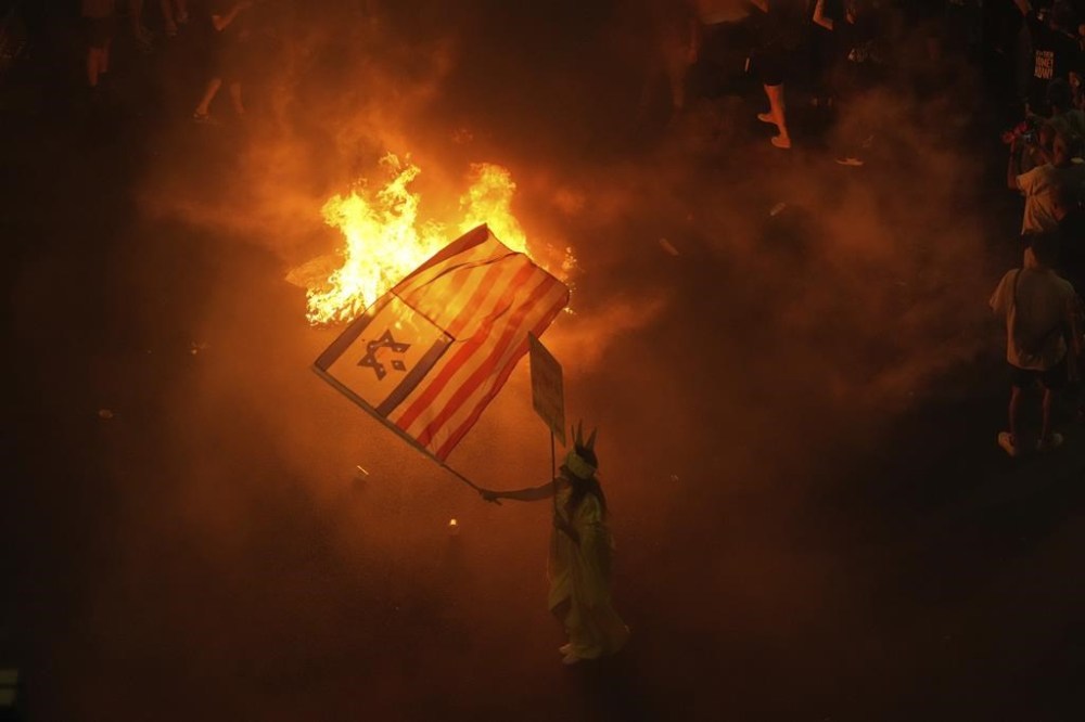 A demonstrator waves the Israeli and U.S. flags during a protest against Prime Minister Benjamin Netanyahu's government and call for the release of hostages held in the Gaza Strip by the Hamas militant group, in Tel Aviv, Israel, Saturday, Sept. 7, 2024. (AP Photo/Ariel Schalit)