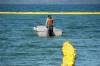 A worker in a small boat drags curtains into place at Clear Lake. (Tim Smith / The Brandon Sun)