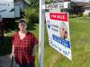 Supplied
                                Roseanne Milburn standing in front of a for sale sign at her home in Elie, Man. Her and her husband, Dan, are moving to Alberta in hopes she’ll be fast-tracked for a double knee replacement, a procedure she’s been waiting on for six years in Manitoba. Her knees cause her excruciating pain and she now relies on walking aids like canes, crutches and walkers. The stress from her condition has also led to permanent hair loss, forcing her to wear wigs and hats in public.