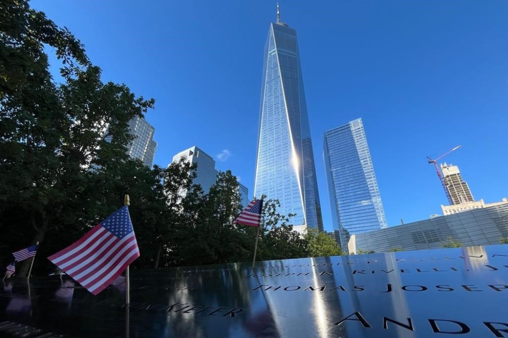 Flags are placed by the names of those killed during the Sept. 11, 2001, attacks at the reflecting pools at the National September 11 Memorial & Museum, Tuesday, Sept. 10, 2024, in New York. One World Trade Center rises in the background. (AP Photo/Donald King)