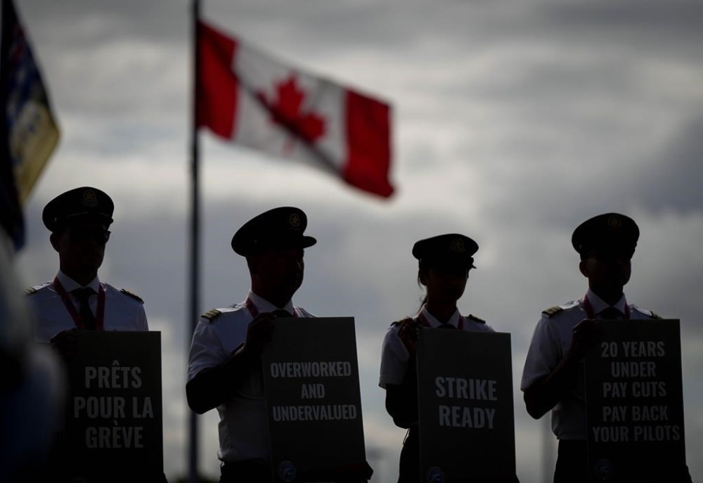 Air Canada pilots air silhouetted while holding signs during an informational picket at Vancouver International Airport in Richmond, B.C., on Tuesday, August 27, 2024.THE CANADIAN PRESS/Darryl Dyck