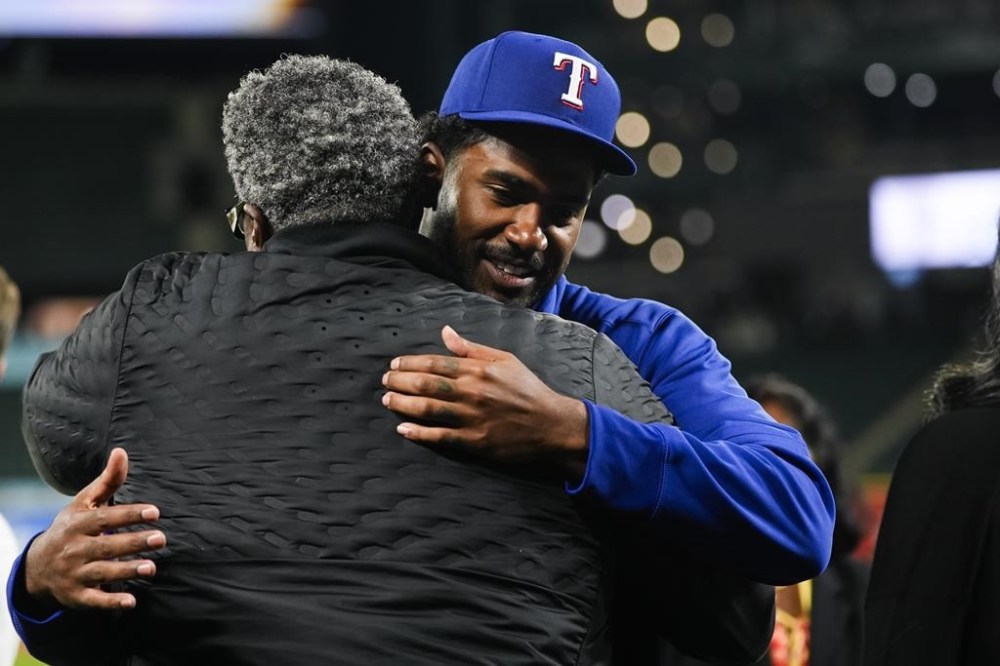 Texas Rangers starting pitcher Kumar Rocker, facing, greets his father and Tennessee Titans defensive line coach Tracy Rocker, after his major league debut in a 5-4 win over the Seattle Mariners in a baseball game Thursday, Sept. 12, 2024, in Seattle. (AP Photo/Lindsey Wasson)