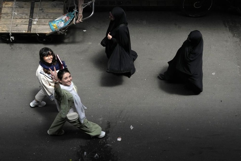 FILE - An Iranian woman without wearing her mandatory Islamic headscarf flashes a victory sign as two head-to-toe veiled women walk at the old main bazaar of Tehran, Iran, June 13, 2024. (AP Photo/Vahid Salemi, File)