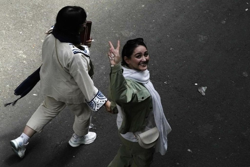 FILE - An Iranian woman without a mandatory headscarf, or hijab, flashes a victory sign as she walks at the old main bazaar of Tehran, Iran, June 13, 2024. (AP Photo/Vahid Salemi, File)