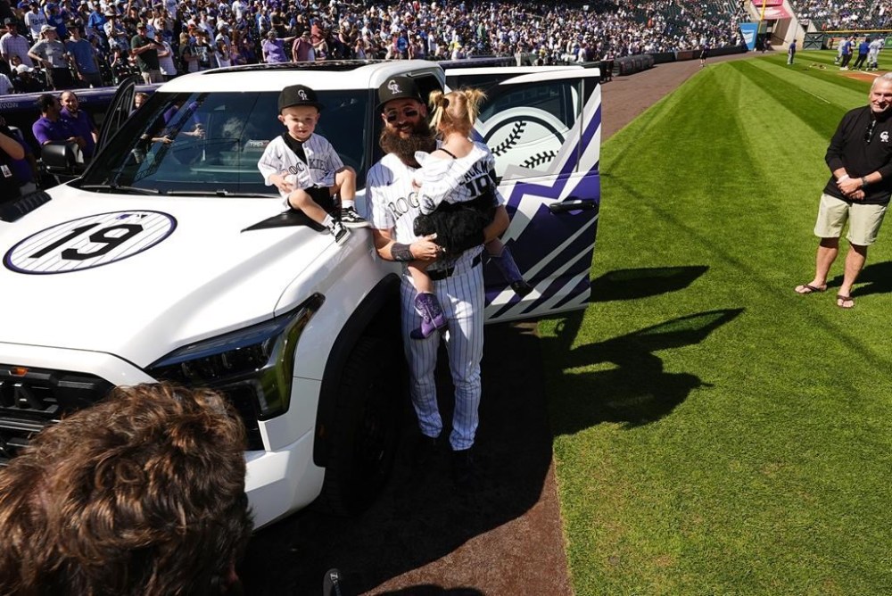 Colorado Rockies center fielder Charlie Blackmon, center, holds his 3-year-old daughter Josie, while his 2-year-old son Wyatt, sits on the hood of a pickup truck given to Blackmon during a ceremony to mark his retirement after 14 seasons as a member of the team before a baseball game against the Los Angeles Dodgers, Sunday, Sept. 29, 2024, in Denver. (AP Photo/David Zalubowski)