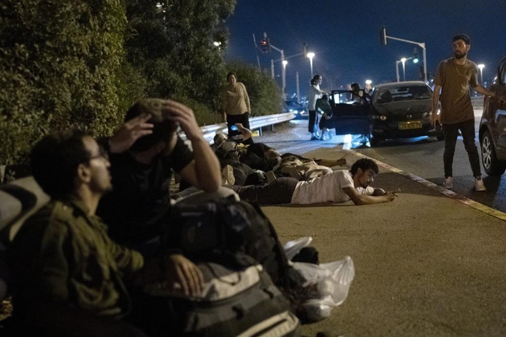 Israelis take cover as projectiles launched from Iran are being intercepted in the skies over in Rosh HaAyin, Israel, Tuesday, Oct. 1, 2024. (AP Photo/Maya Alleruzzo)
