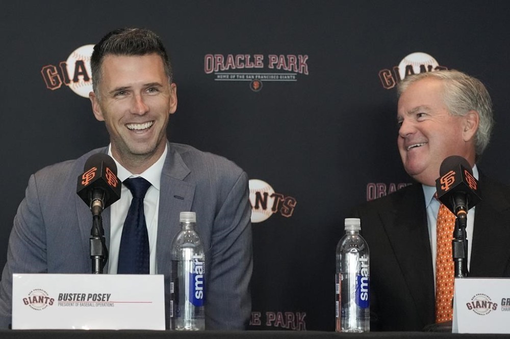 San Francisco Giants president of baseball operations Buster Posey, left, smiles next to chairman Greg Johnson during a news conference in San Francisco, Tuesday, Oct. 1, 2024. (AP Photo/Jeff Chiu)