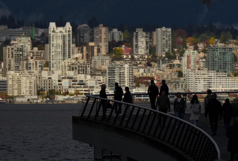 People are silhouetted on a walkway in downtown Vancouver, as condos and apartment buildings in North Vancouver are seen across the harbour, on Tuesday, Oct. 10, 2023. THE CANADIAN PRESS/Darryl Dyck