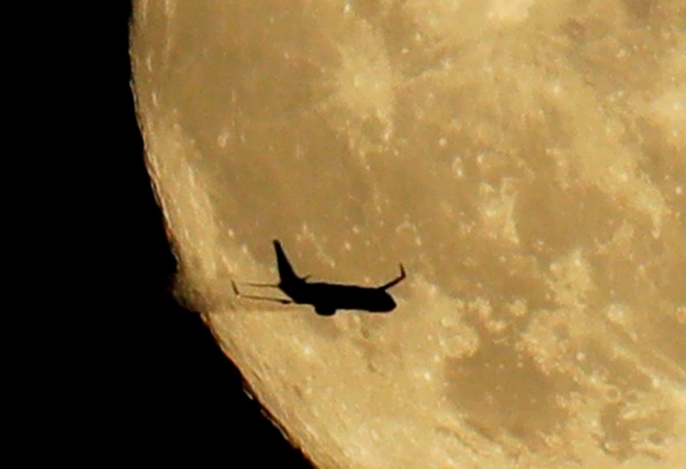 An airplane leaves a vapor trail as it passes in front of a nearly full moon above Tacoma, Wash., Thursday, July 26, 2018. THE CANADIAN PRESS/AP-Ted S. Warren