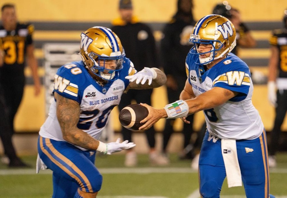 Winnipeg Blue Bombers quarterback Zach Collaros (8) hands off to running back Brady Oliveira (20) during first half CFL football game action against the Hamilton Tiger-Cats in Hamilton, Ont. on Friday, October 4, 2024. THE CANADIAN PRESS/Peter Power