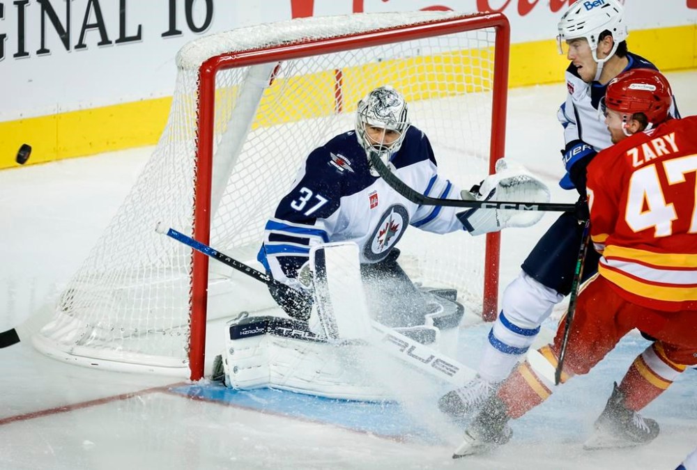 Winnipeg Jets' goalie Connor Hellebuyck, left, guards the net as Calgary Flames' Connor Zary, right, is checked by Haydn Fleury during third period NHL pre-season hockey action in Calgary on Friday, Oct. 4, 2024.THE CANADIAN PRESS/Jeff McIntosh