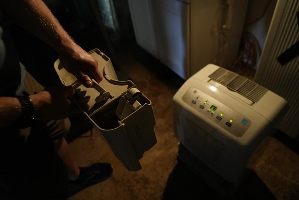 Travis Edwards retrieves water from his basement humidifier to use for flushing toilets Thursday, Oct. 3, 2024 in Asheville, North Carolina. (AP Photo/Brittany Peterson)